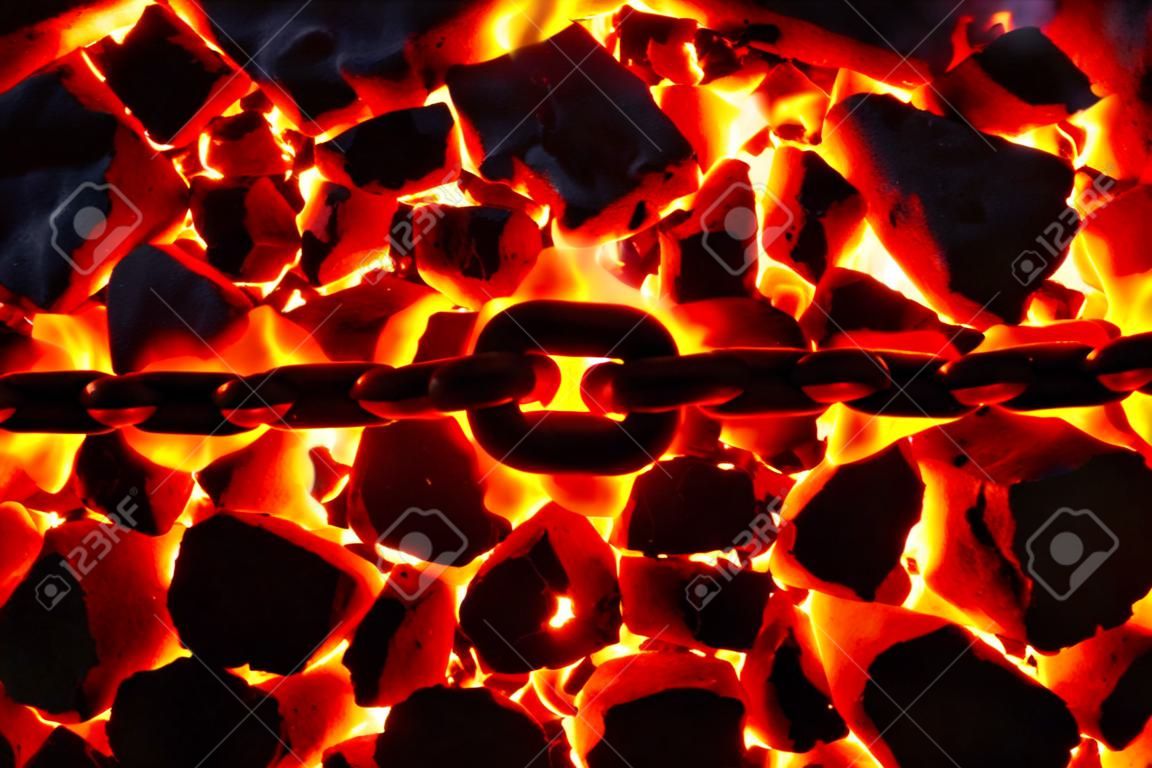 Die Glieder einer glühenden Kette liegen auf einem brennenden Kohleanthrazit.
