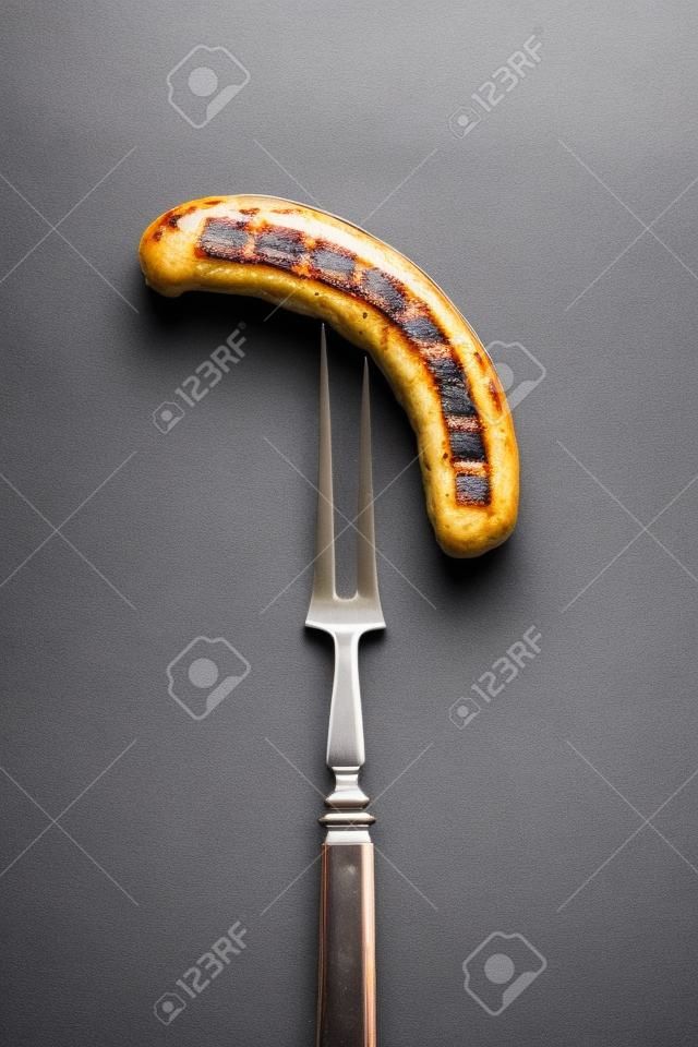 Grilled Bavarian sausage on a fork. Copy space.