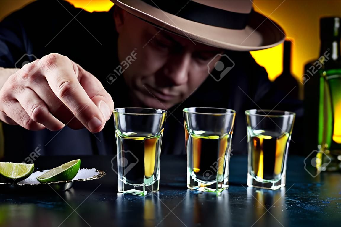 Mężczyzna w kapeluszu pije tequilę z plasterkami soli i limonki. selektywne skupienie.
