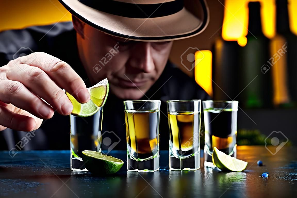 Mann mit Hut trinkt Tequila mit Salz und Limettenscheiben. Selektiver Fokus.