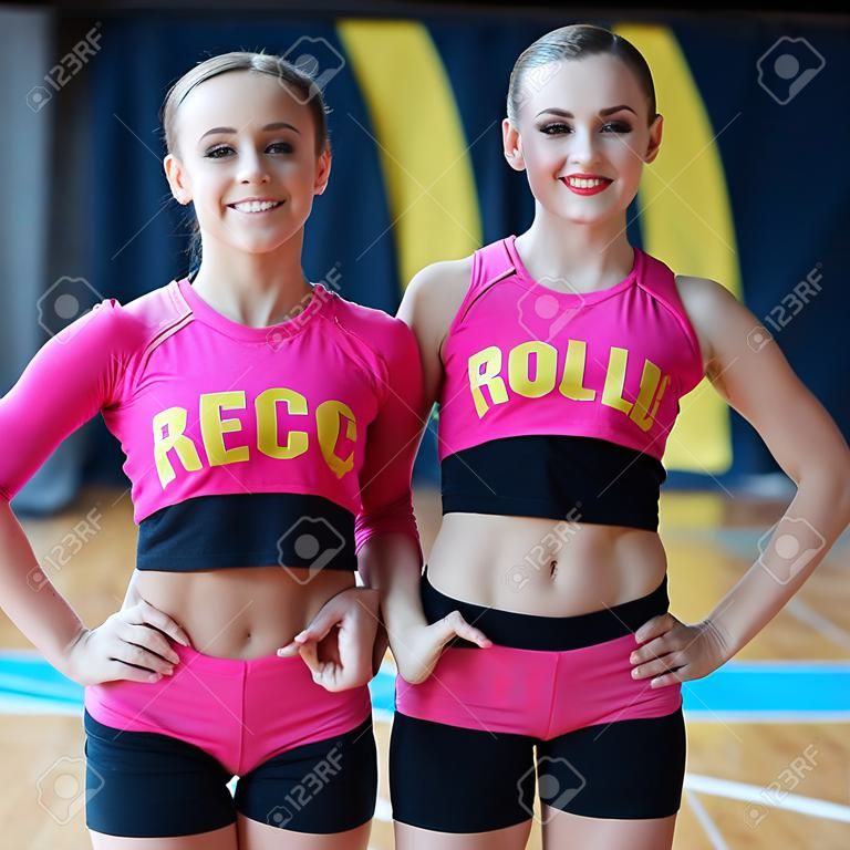 girls with fit body demonstrating muscles, smiling beautiful women in black and pink sportswear looking at camera, cheerleaders working out in sports club, cheerleaders smiling and posing at camera