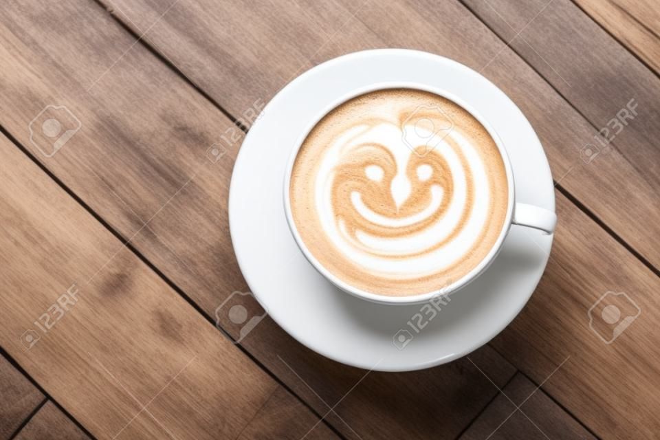 Top view white cup of latte art happy smile face on brown wooden table background wite copyspace.