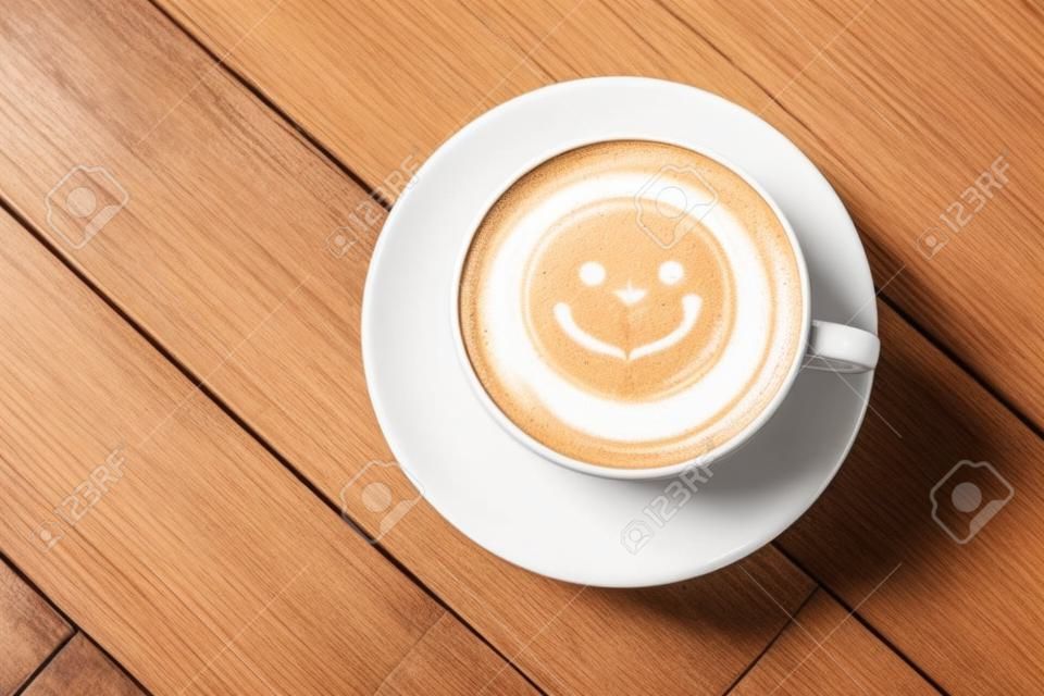 Top weiß Tasse Latte Art glücklich Lächeln Gesicht auf braunem Holztisch Hintergrund Wite Exemplar.