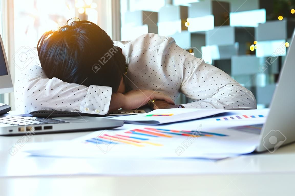 Zmęczony biznesmen przepracowany śpi nad laptopem w biurku w pracy w swoim biurze.
