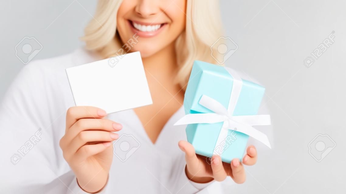 Glückliche lächelnde Frau, die weiße leere Karte und Geschenkbox hält. Leere Karte zum Anpassen von Text.