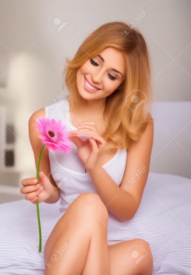 Beautiful young woman in bed holding a gerbera flower