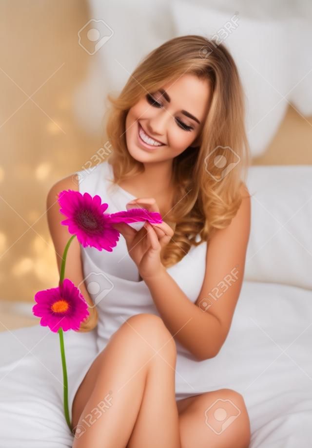 Beautiful young woman in bed holding a gerbera flower
