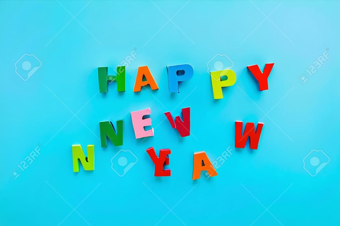 Text Happy New Year of bright multicolored wooden letters on blue background. Top view Greeting card
