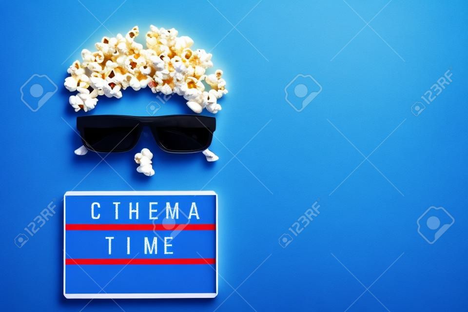 Abstract image of viewer, 3D glasses, popcorn and light box text Cinema time on blue paper background. Concept cinema movie and entertainment Flat lay Top view Copy space for text or your design.