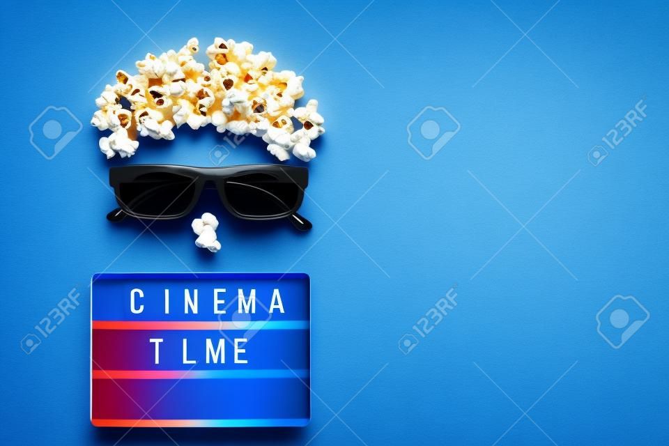 Abstract image of viewer, 3D glasses, popcorn and light box text Cinema time on blue paper background. Concept cinema movie and entertainment Flat lay Top view Copy space for text or your design.