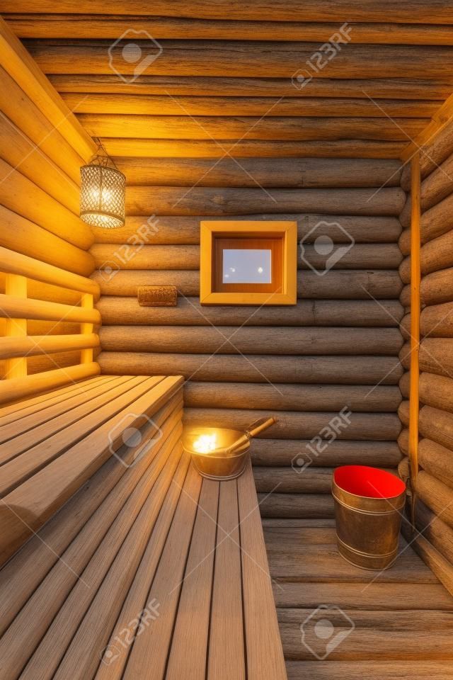 Tradicional sauna rusa con el registro de bancos de madera, termómetro, la lámpara y la ventana con cuchara de madera y baño de escoba en el banco