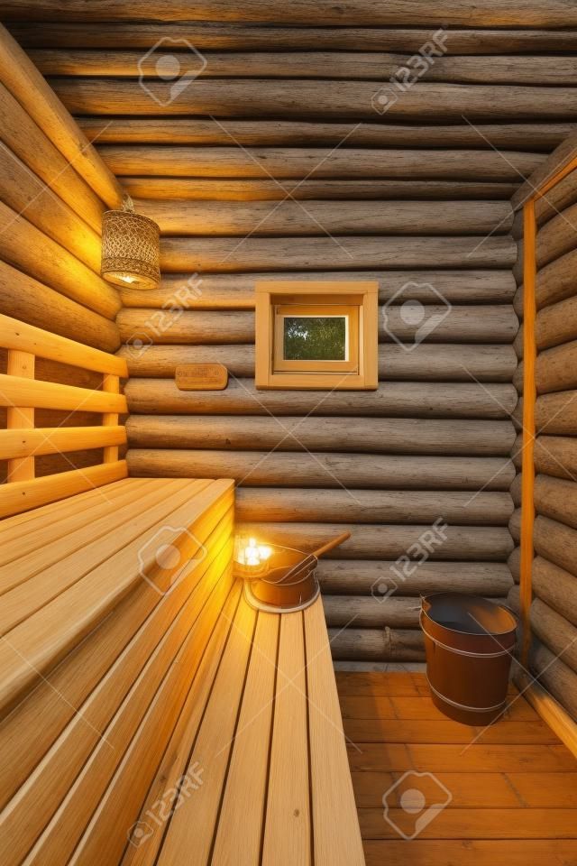 Traditional Russian log sauna with wooden benches, thermometer, lamp and window with wooden bucket and bathing broom on bench
