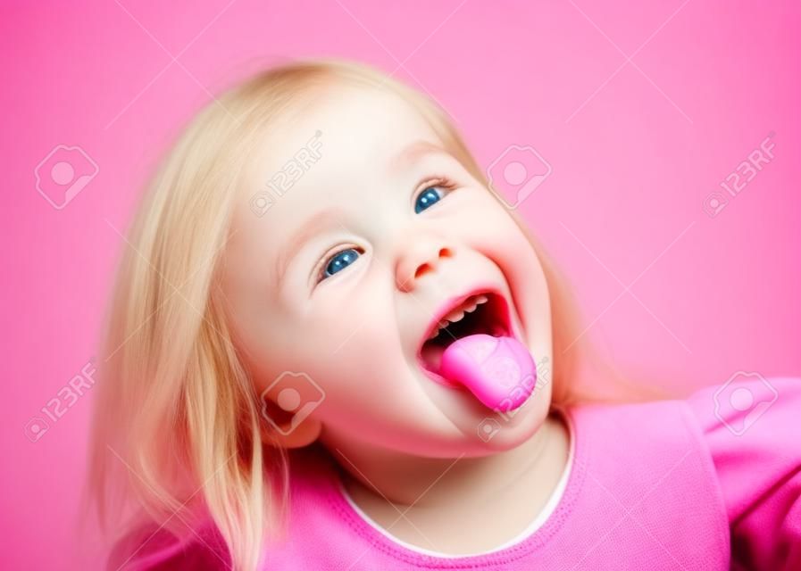 Nahaufnahme eines kleinen Mädchens mit herausgestreckter Zunge über rosa isoliert.