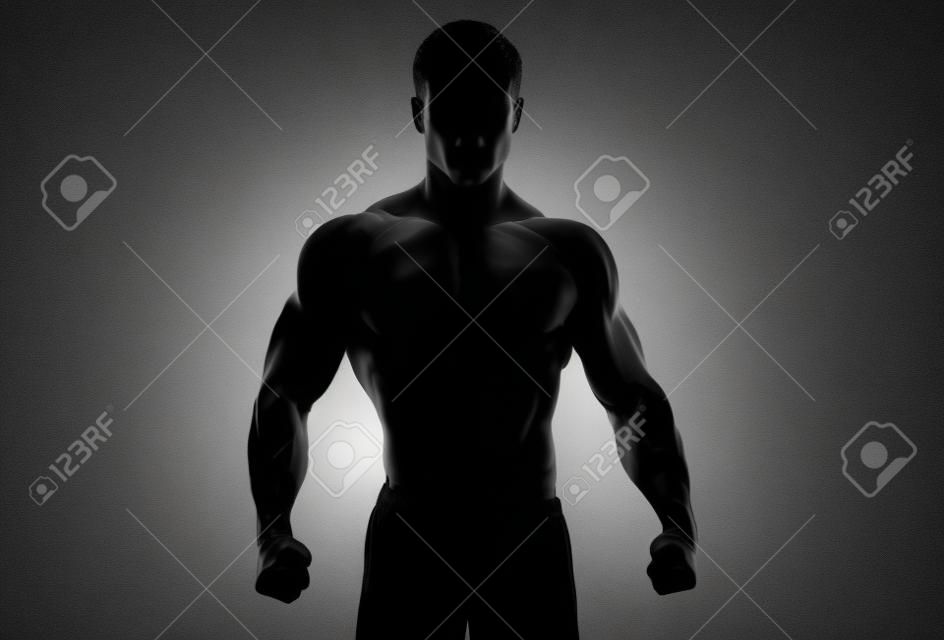 Темный силуэт сильного человека на белом фоне. Уверенный молодой фитнес человек с сильными руками и сжатыми кулаками. Отсечения путь внутри