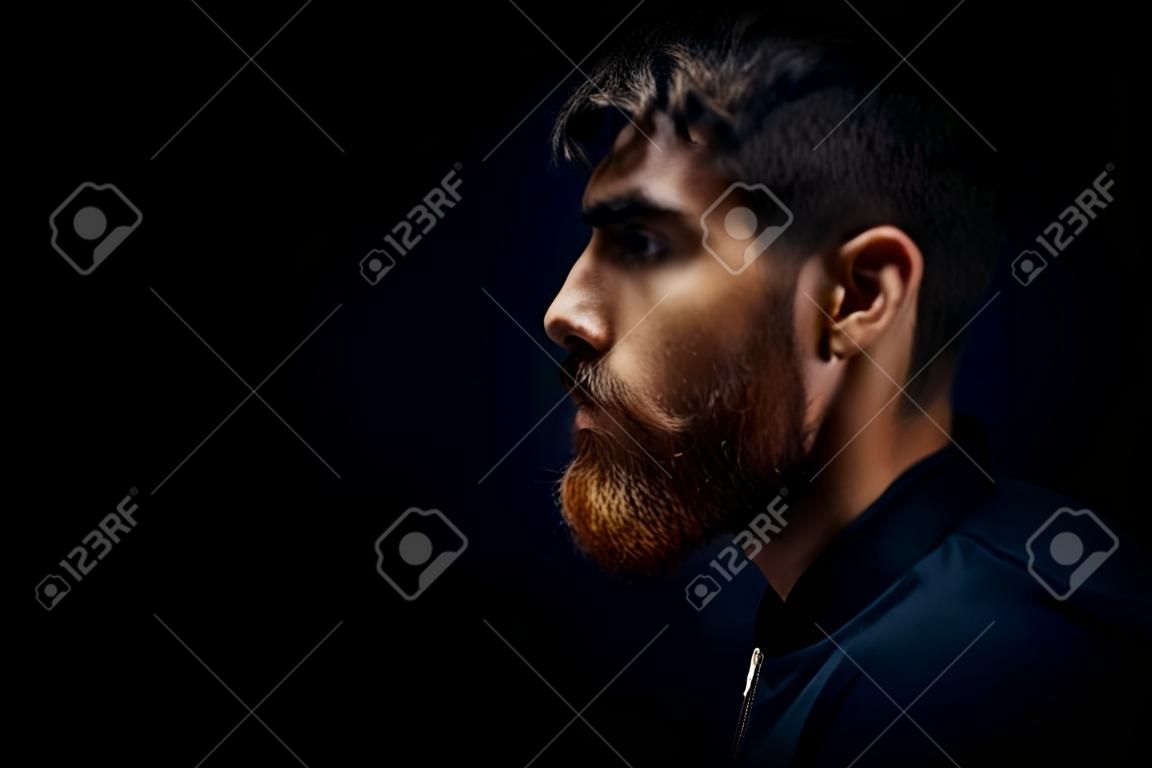 Close-up image of serious brutal bearded man on dark background Confident and dramatic concept