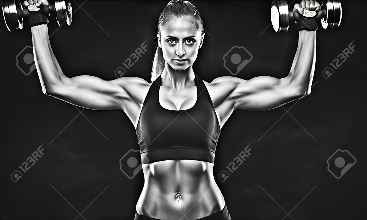 Colpo in bianco e nero di giovane bodybuilder femminile che lavora con pesi a mano e pantaloncini curling manubri su sfondo nero Caucasica donna con corpo muscoloso, abs Mockup.