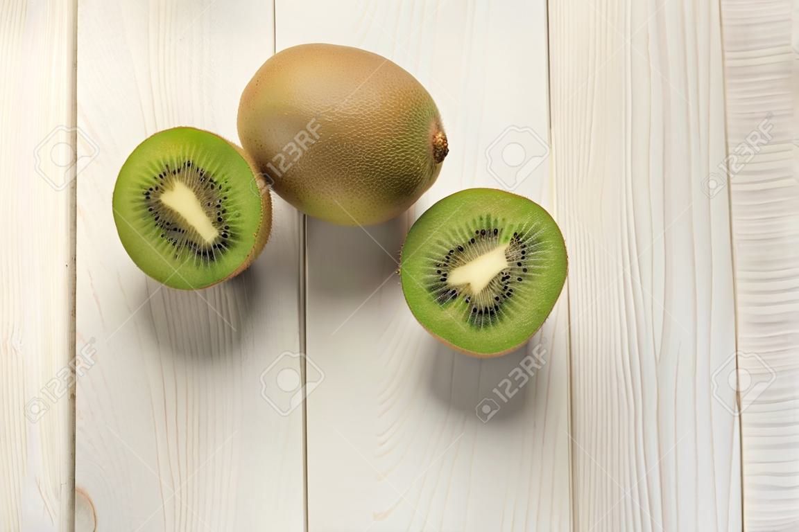 One open kiwi and one whole on white wooden background, fresh fruit