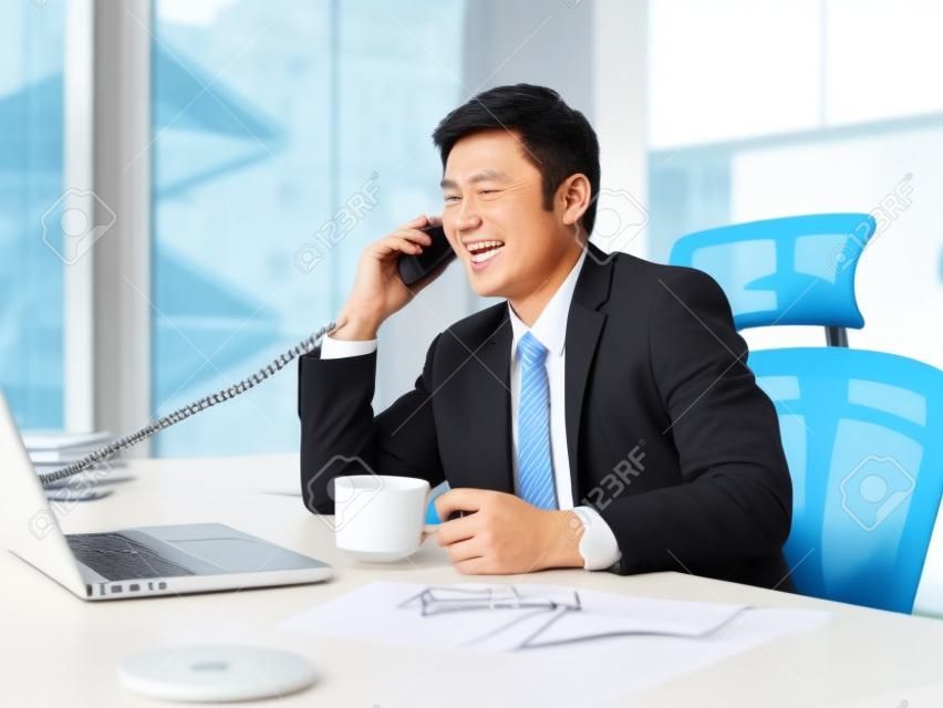 Hombre de negocios asiático hablando por teléfono en la oficina, mirando feliz