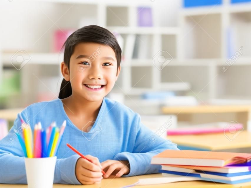 studente asiatico felice della scuola elementare che studia in aula che guarda l'obbiettivo che sorride,