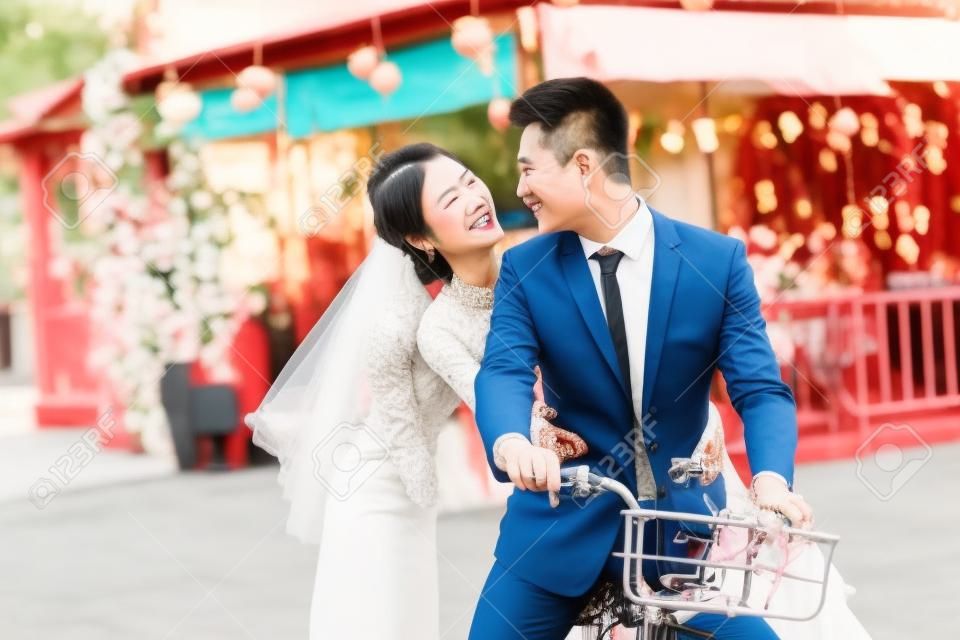 浪漫亚洲新婚夫妇开心在一起骑自行车。