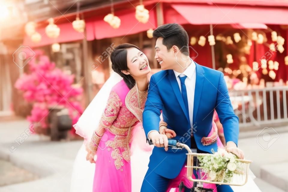 浪漫亚洲新婚夫妇开心在一起骑自行车。
