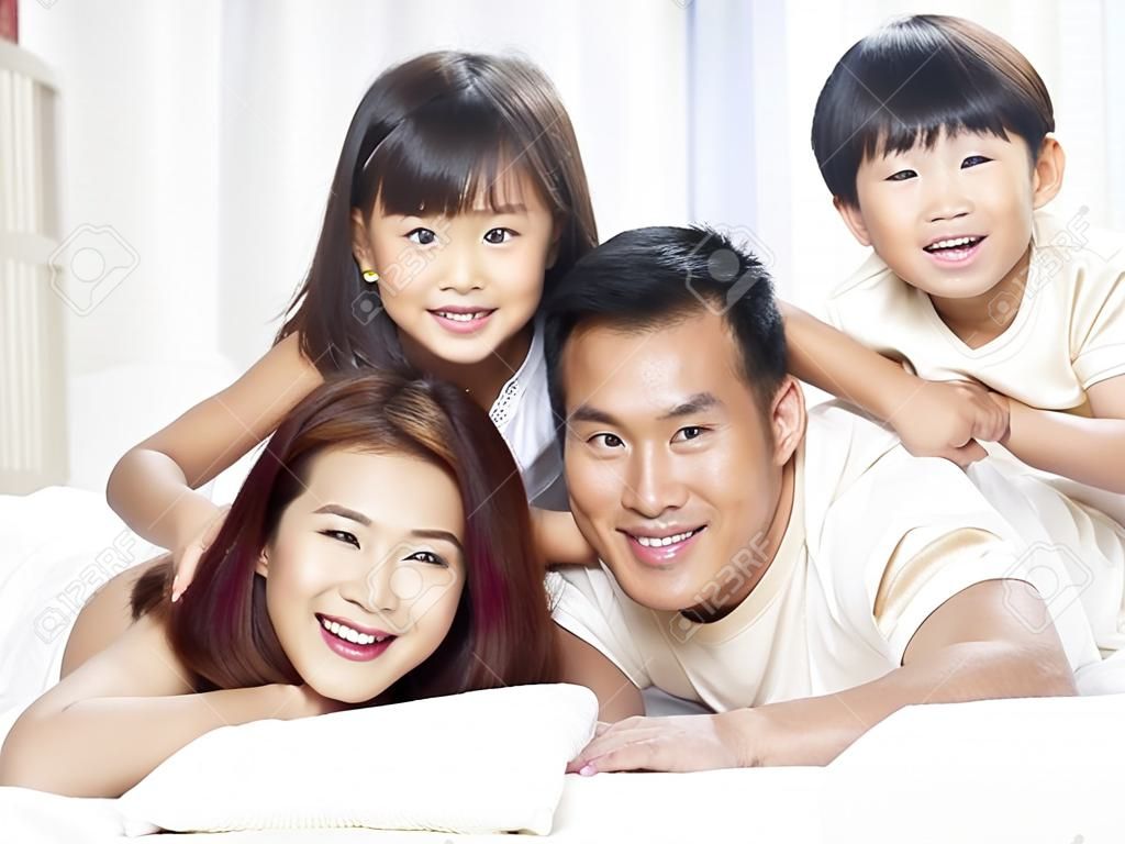 Família asiática feliz com duas crianças que se divertem na cama em casa.
