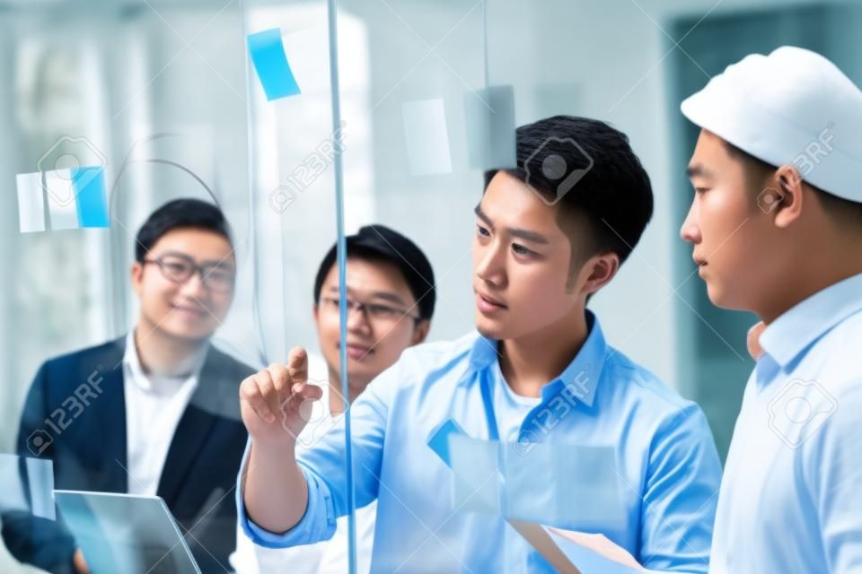 joven empresario asiático de una pequeña empresa dibujando un diagrama sobre vidrio durante un taller de equipo en la oficina discutiendo y formulando estrategias comerciales.