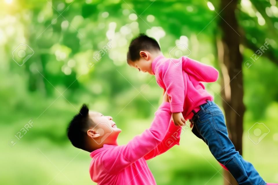 cute little asian boy lifted by father outdoors in park