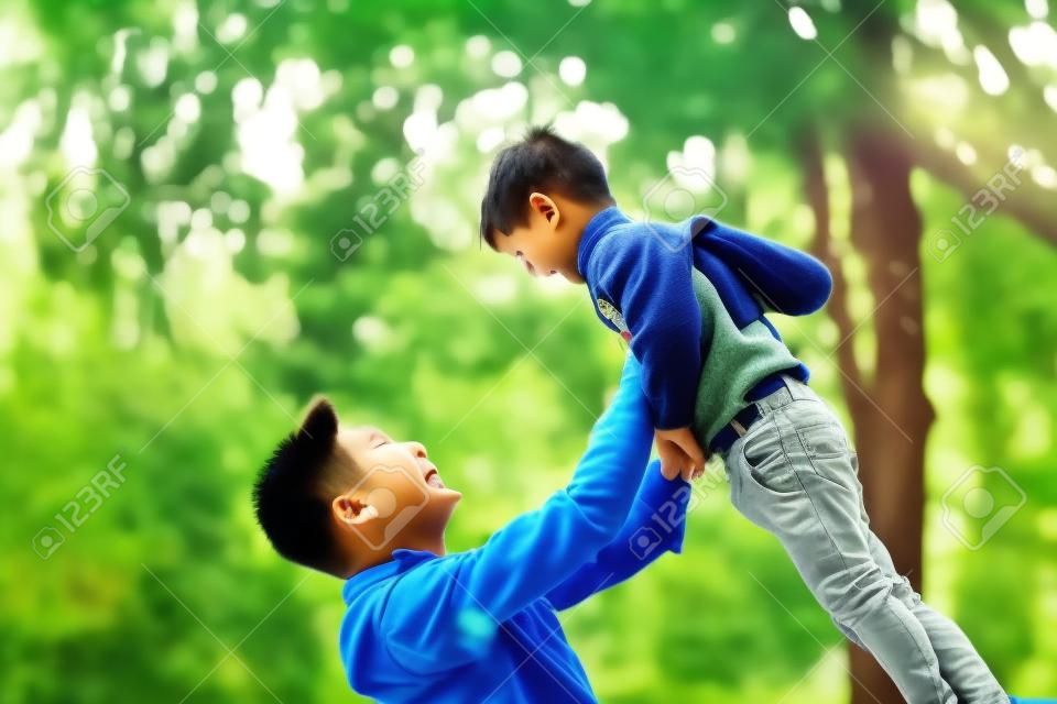 cute little asian boy lifted by father outdoors in park