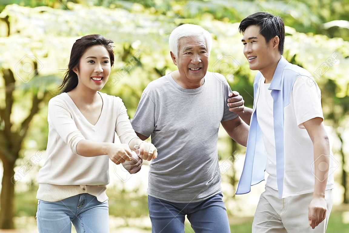 young asian couple helping father stand up and walk outdoors in park