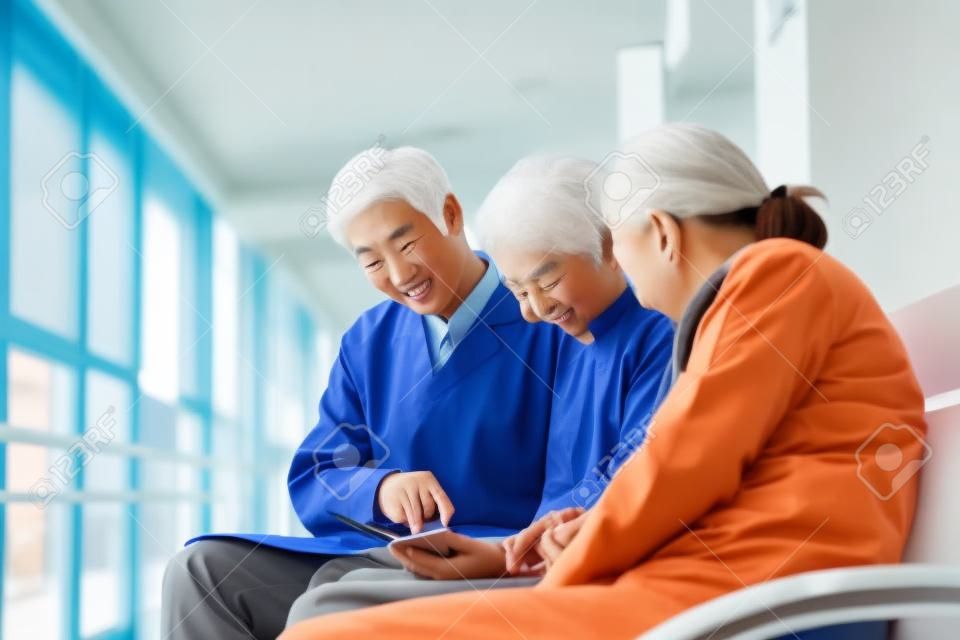 젊은 아시아 의사는 병원 복도에서 디지털 태블릿을 사용하여 노인 부부 환자와 테스트 결과 및 진단에 대해 논의합니다.