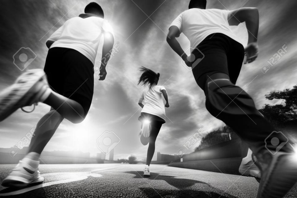 tres jóvenes adultos asiáticos corriendo al aire libre, vista trasera y de ángulo bajo, blanco y negro