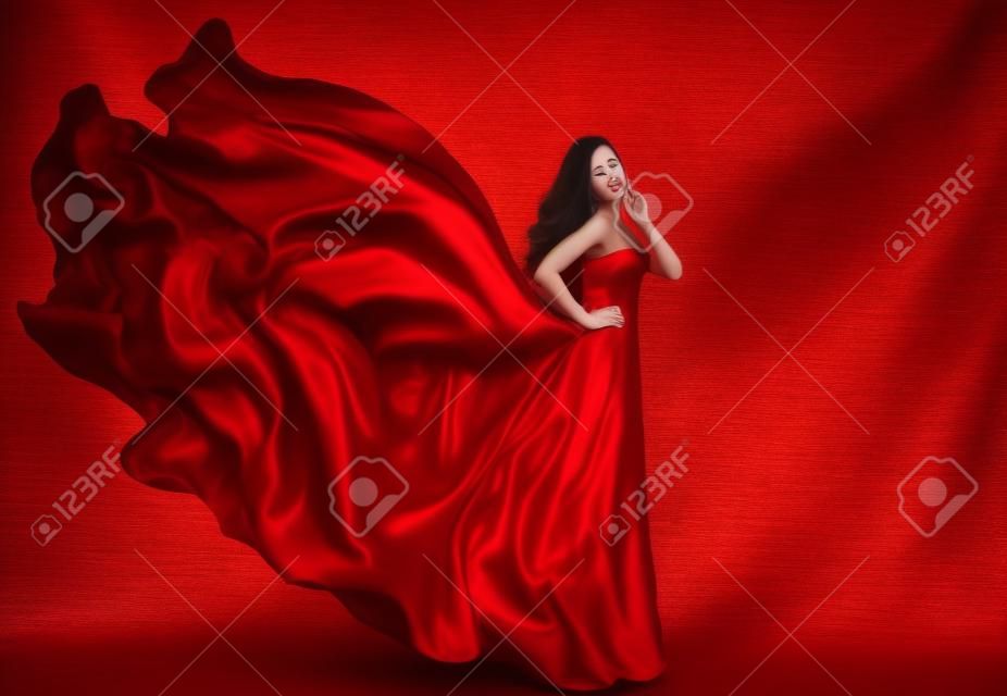 Vestido vermelho da mulher, modelo de moda em vestido de seda longo acenando no vento, menina de fantasia em tecido voador.