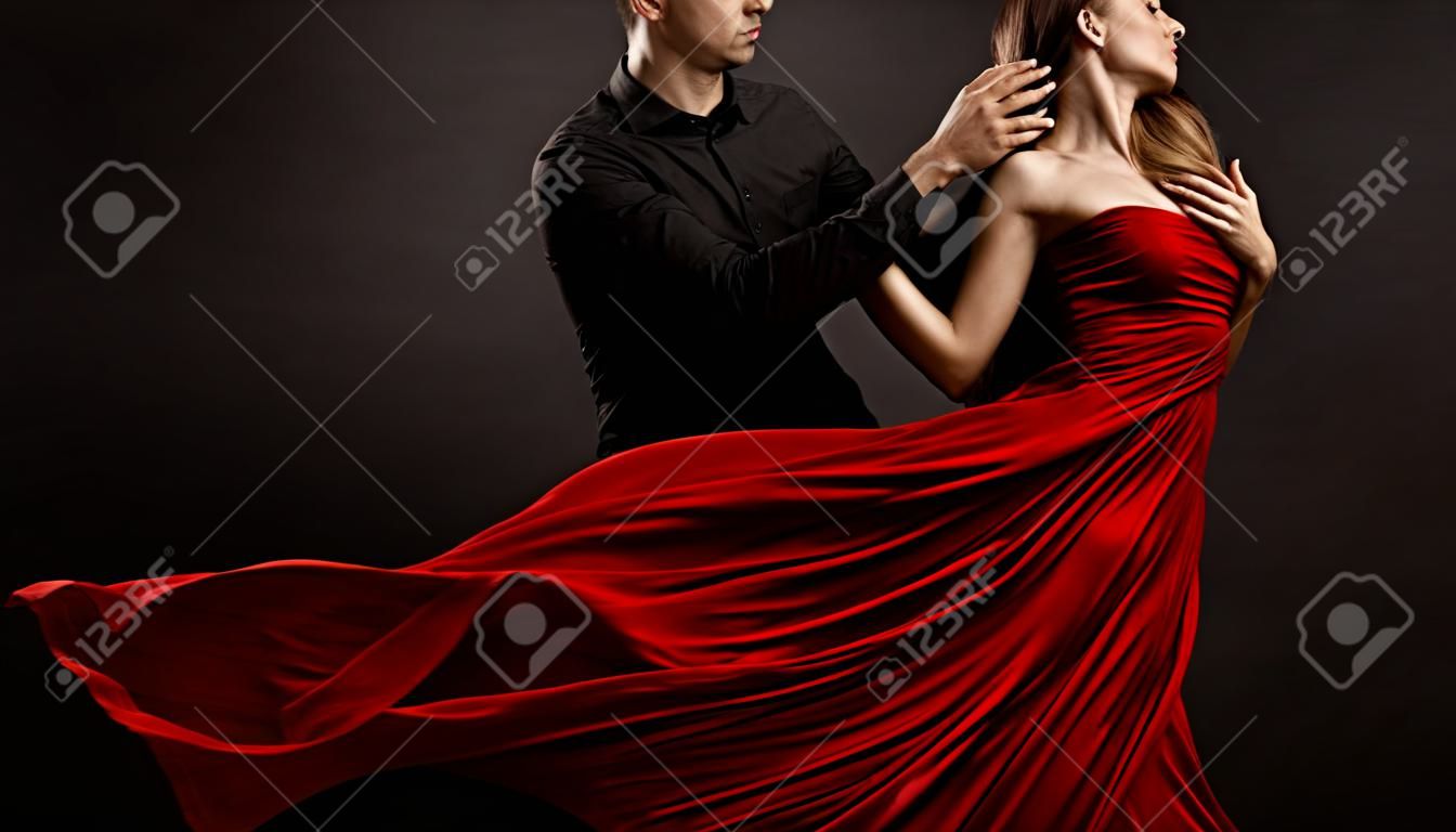 Coppia di amanti romantici che ballano. Uomo che abbraccia e bacia bella donna in abito volante rosso di seta. Ritratto di moda. Sfondo nero da studio