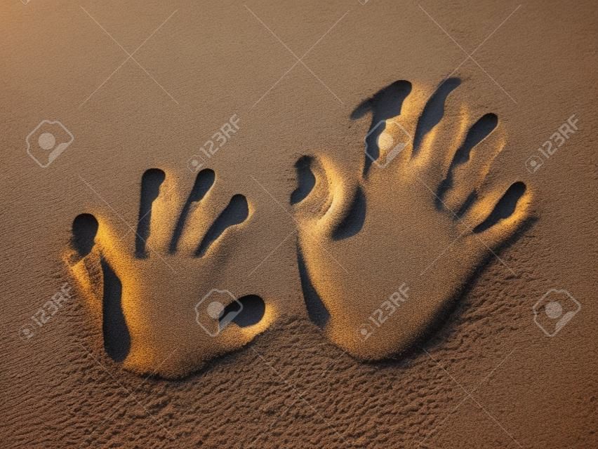 Optische Täuschung - Handabdrücke eines Kindes und eines Erwachsenen im Sand