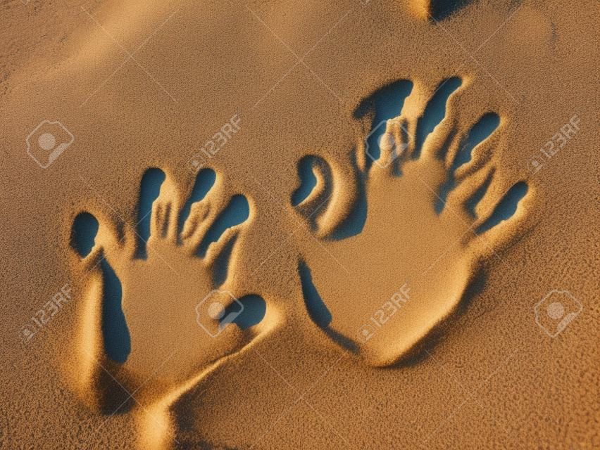 Optische Täuschung - Handabdrücke eines Kindes und eines Erwachsenen im Sand