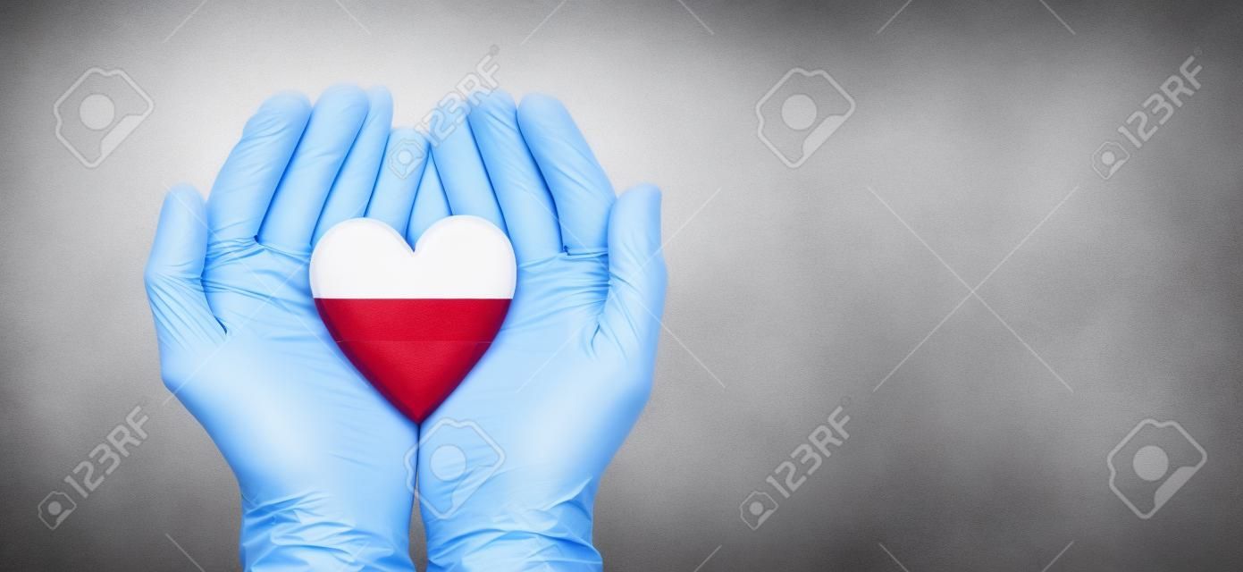Mani dei medici che indossano guanti chirurgici che tengono il cuore della bandiera della Lettonia