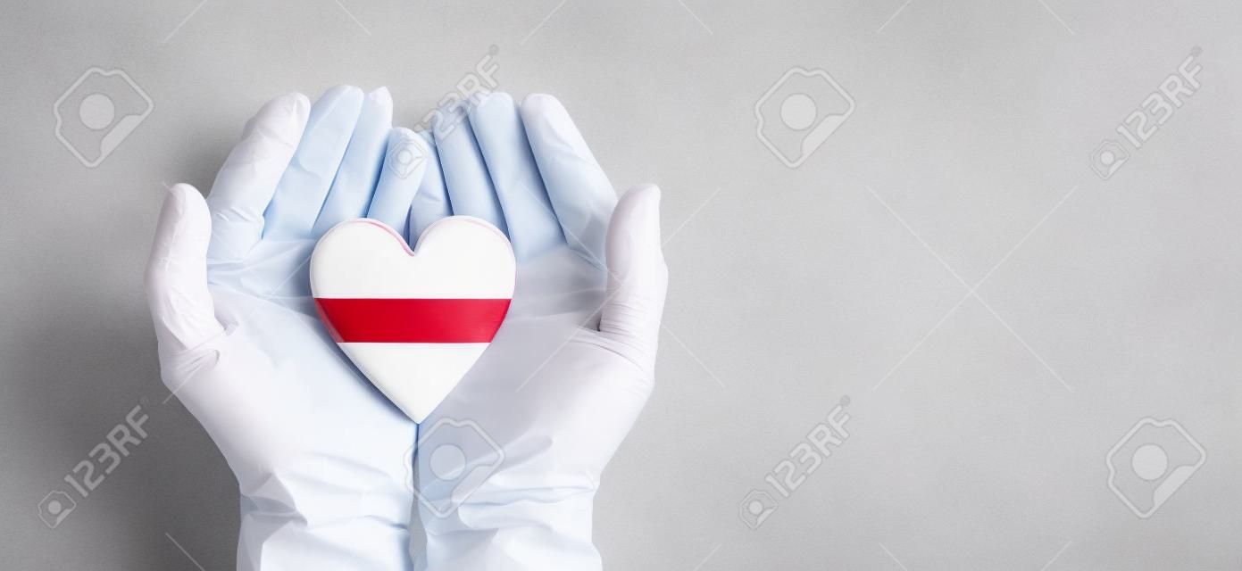 Doctors hands wearing surgical gloves holding Latvia flag heart
