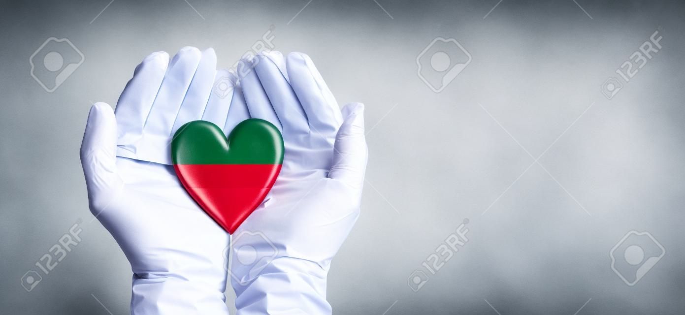 Mani dei medici che indossano guanti chirurgici che tengono il cuore della bandiera della Lettonia