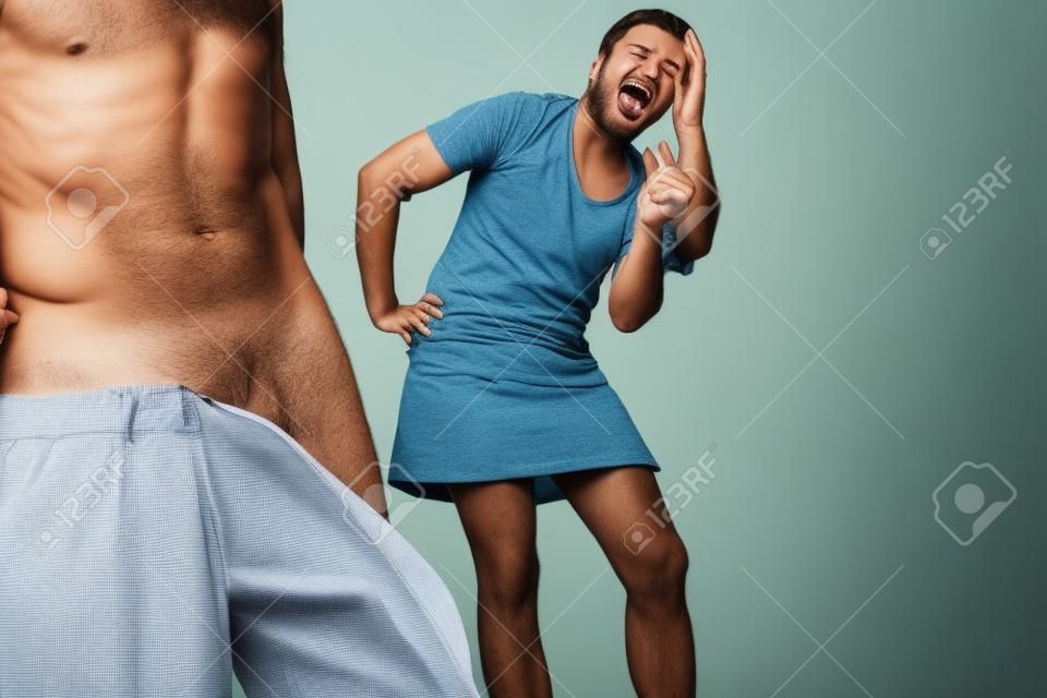 peinlich Mann mit heruntergelassenen Hosen, während Frau macht sich lustig über seine Männlichkeit