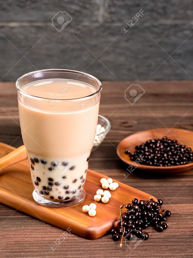 Köstlicher Schaummilchtee mit Tapiokaperlenkugel in Glas auf Holztisch und dunkelgrauem Ziegelsteinhintergrund, beliebtes Essen und Trinken in Taiwan, Nahaufnahme