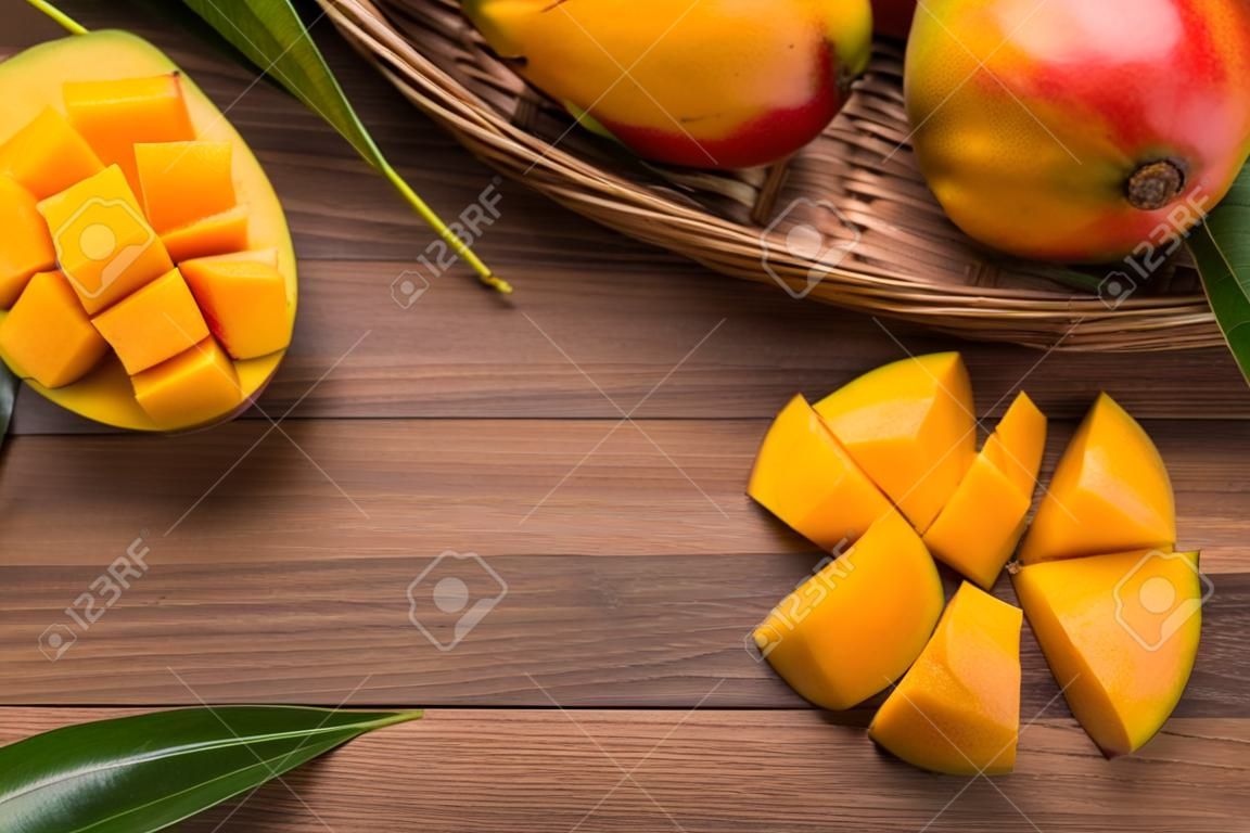 Mango. Close up of fresh ripe mango fruit with leaves over dark wooden table background with green leaves.