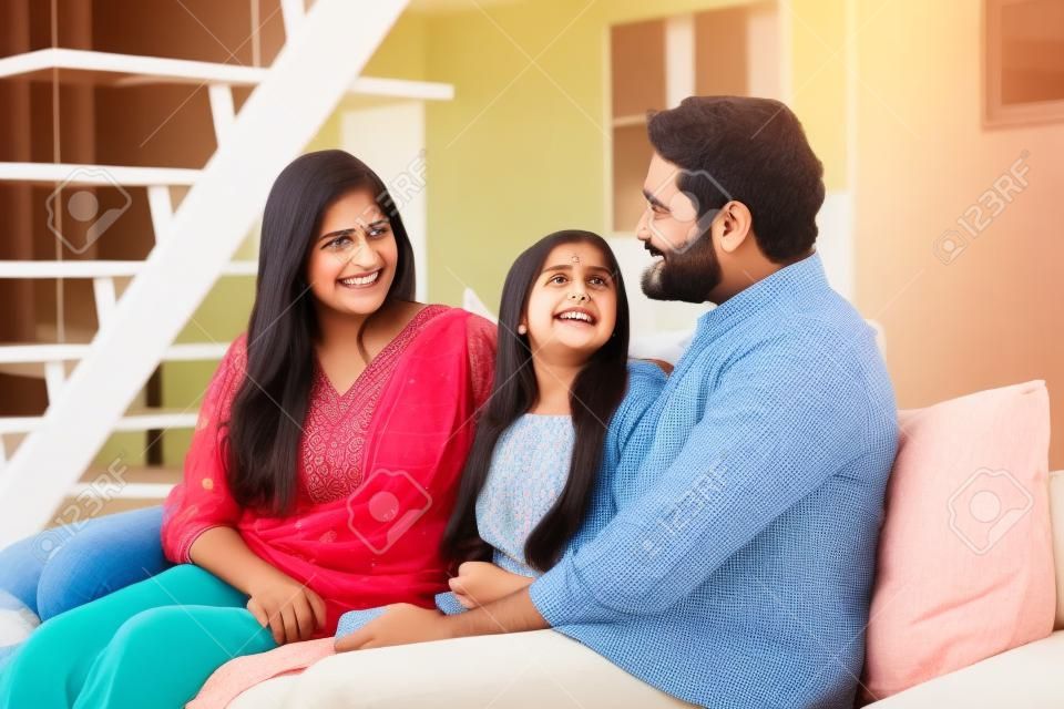 Szczęśliwa indyjska rodzina z nastoletnią córką rozmawiającą siedząc na kanapie w domu.