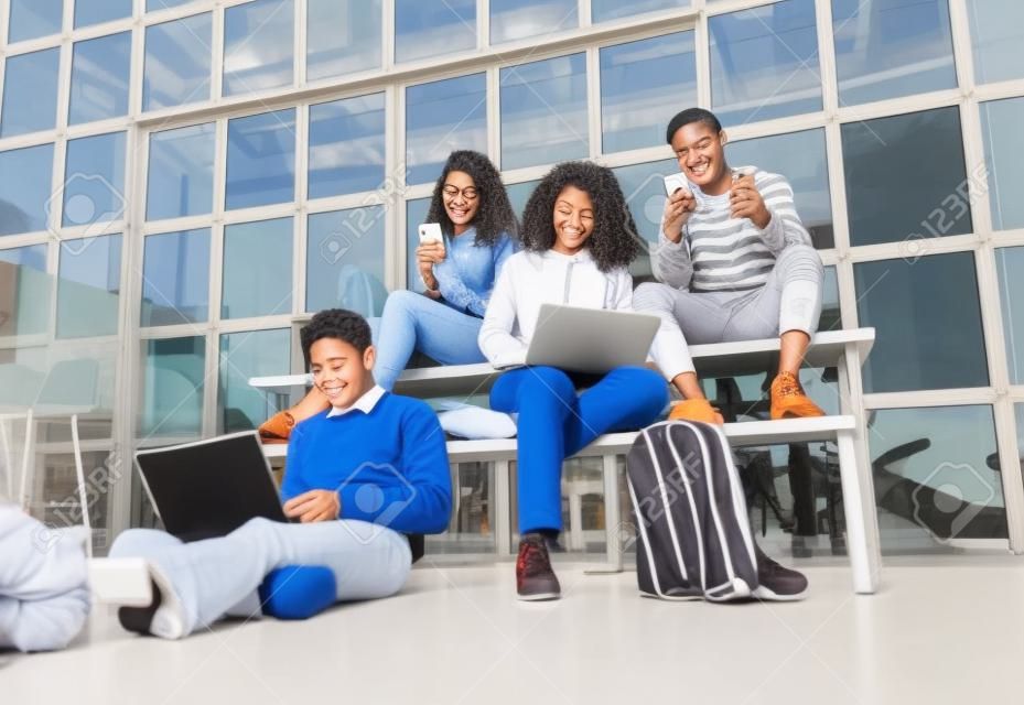 Multiculturele studenten op de middelbare school campus met behulp van gadgets.