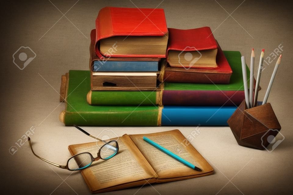 Stack of old books, textbook, glasses and pencils in office background for education retro concept