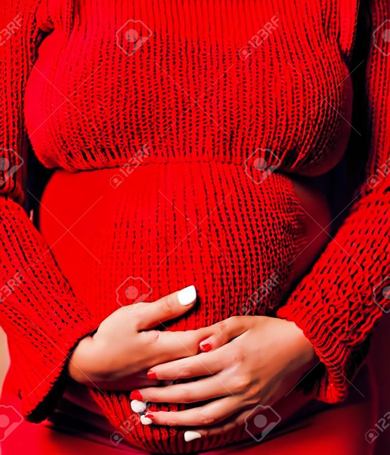 Nahaufnahme Porträt einer schwangeren Frau mit dickem Bauch, Hände halten, roter Pullover im Hintergrund, Wahl des Geschlechts, Lifestyle-Menschen-Konzept