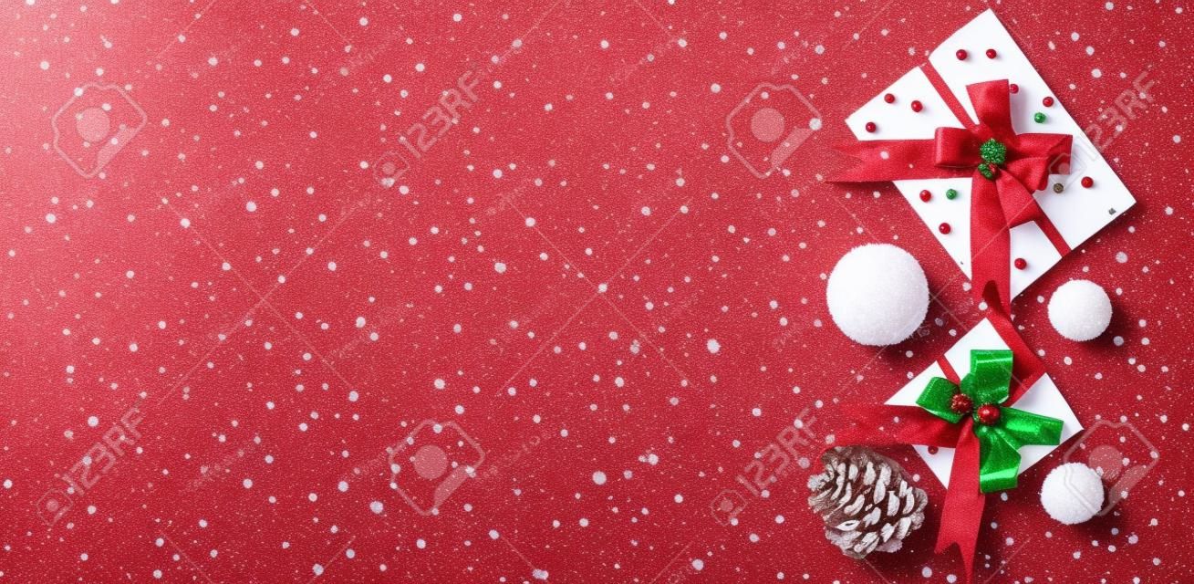Buon Natale e buone feste biglietto di auguri, cornice, banner, pigna e palle di neve decorative su sfondo rosso, vista dall'alto. Tema delle vacanze invernali. Disposizione piatta