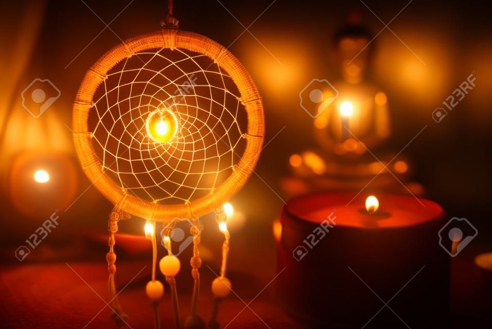 Vintage style image of dreamcatcher and candle light with blurred Buddha statue on the background.
