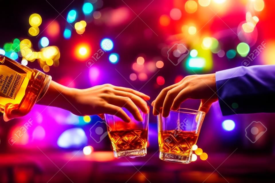 金貨カラフルな背景の仕事の後、パーティーの夜にバーボンウイスキーの飲み物を持つ友人の歓声