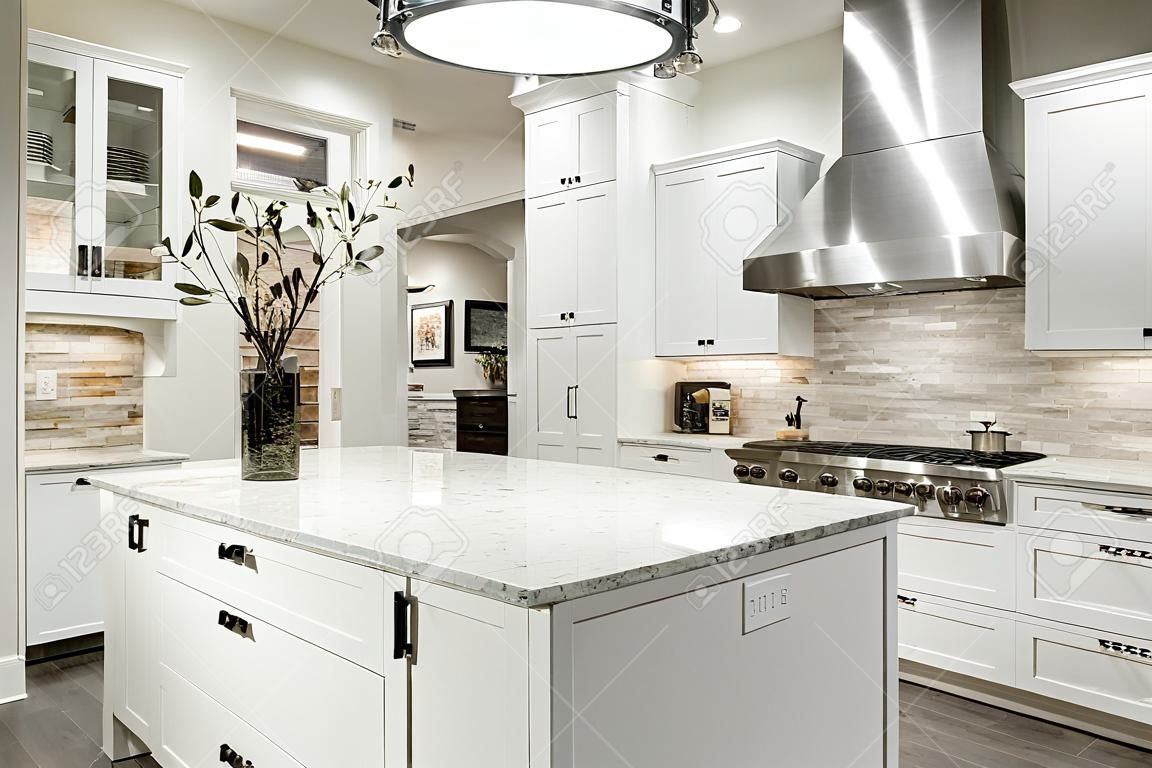 Cozinha gourmet apresenta armários shaker branco com bancadas de mármore, pedra backsplash de telha do metrô, porta dupla geladeira de aço inoxidável e linda ilha de cozinha.